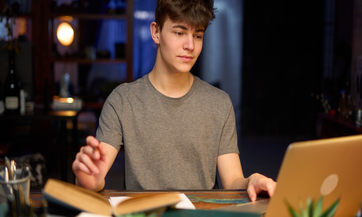 Teenage student learning at home with books and laptop computer